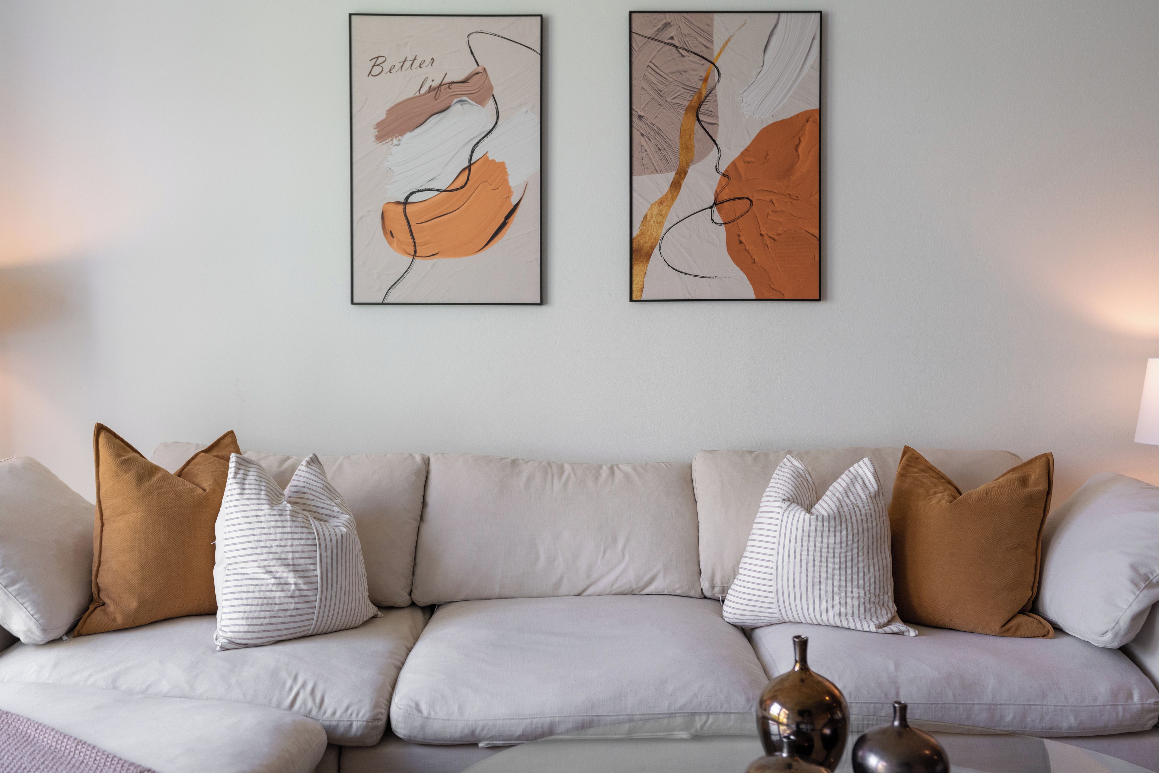 A neutral-toned sofa with striped and solid pillows, two abstract paintings on the wall, and a small table with decorative vases.