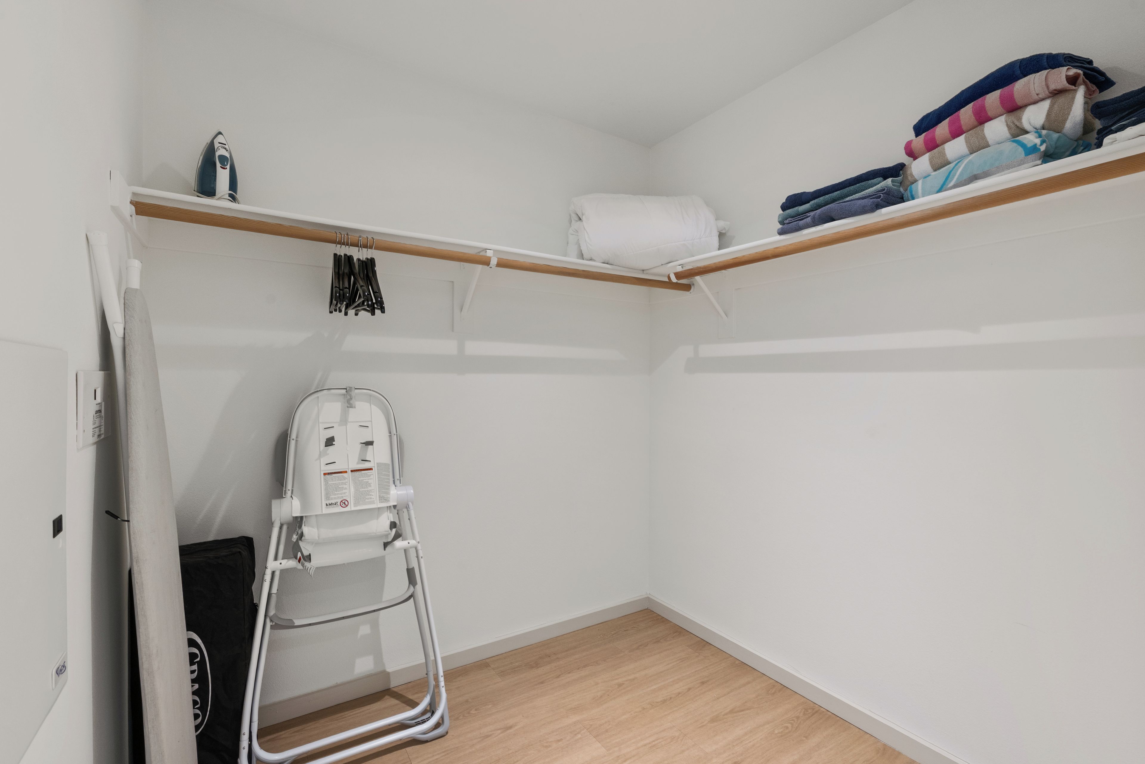 Ein kleiner, kompakter Raum mit Holzboden, weißer Wand und einem Holzregal mit gefalteter Kleidung.