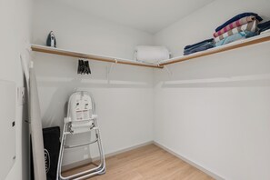 A small, compact room with a wooden floor, a white wall, and a wooden shelf with folded clothes.