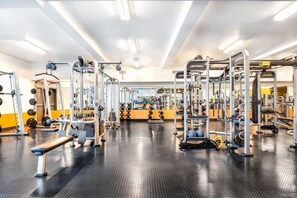 Une salle de sport équipée de divers appareils d’exercice, d’un banc et d’un mur recouvert de miroirs.