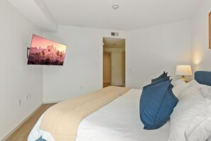 Een hotelkamer met een bed, een aan de muur bevestigde televisie, een lamp en een deur naar een andere kamer.