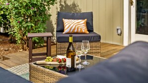 A wicker table with a bottle of wine, two glasses, and a plate of food on a deck. - Boutique UO Stay • Epic Game Room • Walk to Autzen (Eugene)