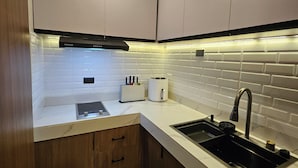 Una cocina compacta con armarios blancos, un lavamanos negro y una encimera blanca.