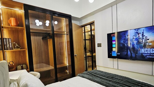 Una habitación de hotel moderna con una cama grande, un televisor montado en la pared, un armario de madera y una lámpara en el techo.