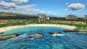 Un complejo turístico costero con playa de arena, aguas azules cristalinas y un edificio grande de varios pisos.