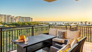 Un balcón con mobiliario de mimbre, una mesa y vistas al océano y edificios.