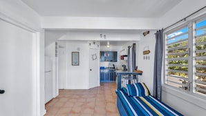 Una habitación luminosa y amplia con una cama grande, vistas al exterior y una cocina al fondo.