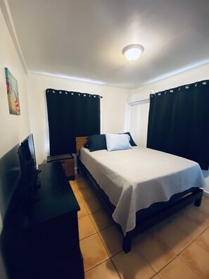A small, clean room with a bed, a desk, and a window with curtains.