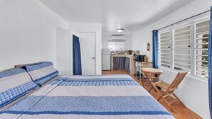 Quarto com cama, pequeno espaço de cozinha e área de refeições com mesa e cadeiras.