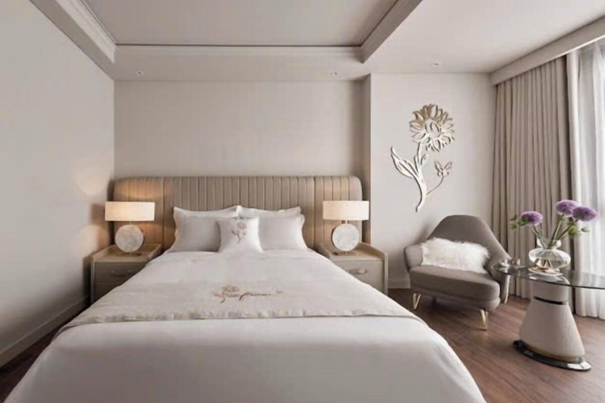 A hotel room with a large bed, two bedside tables with lamps, a chair, and a decorative wall piece.