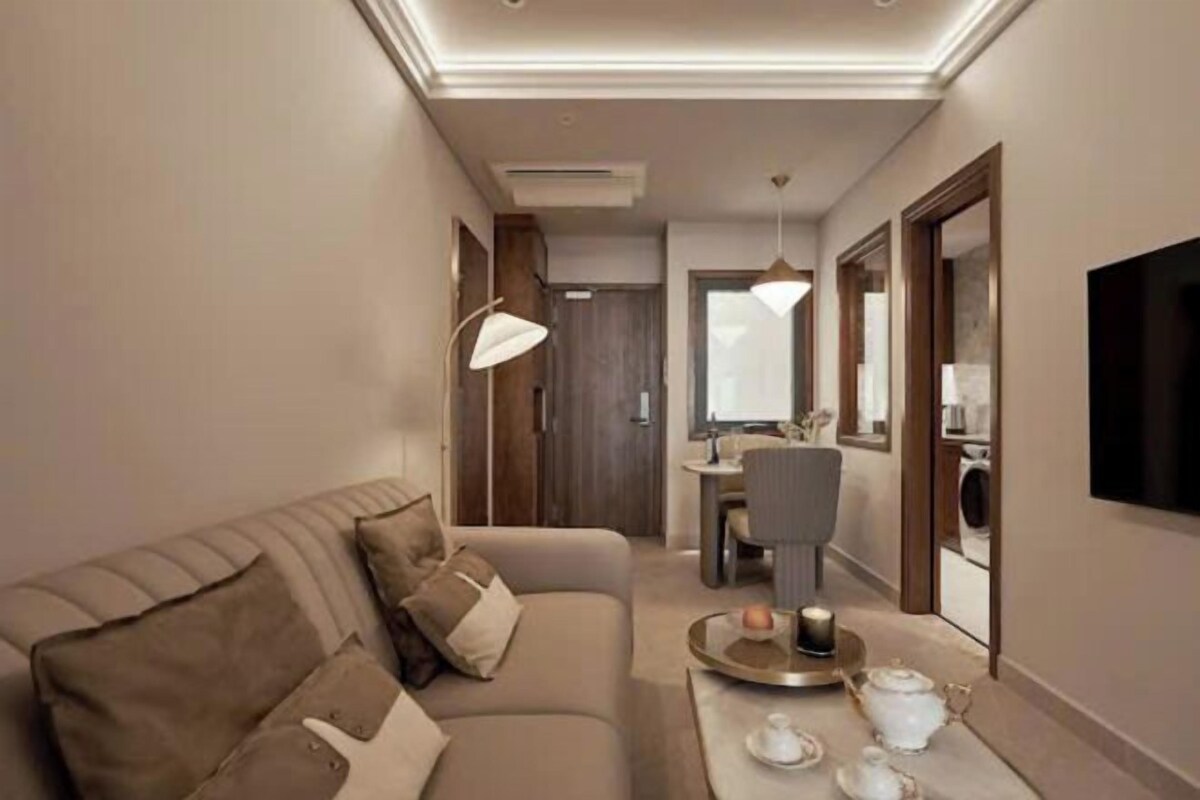 A modern living room with a sofa, a dining area, and a TV mounted on the wall.