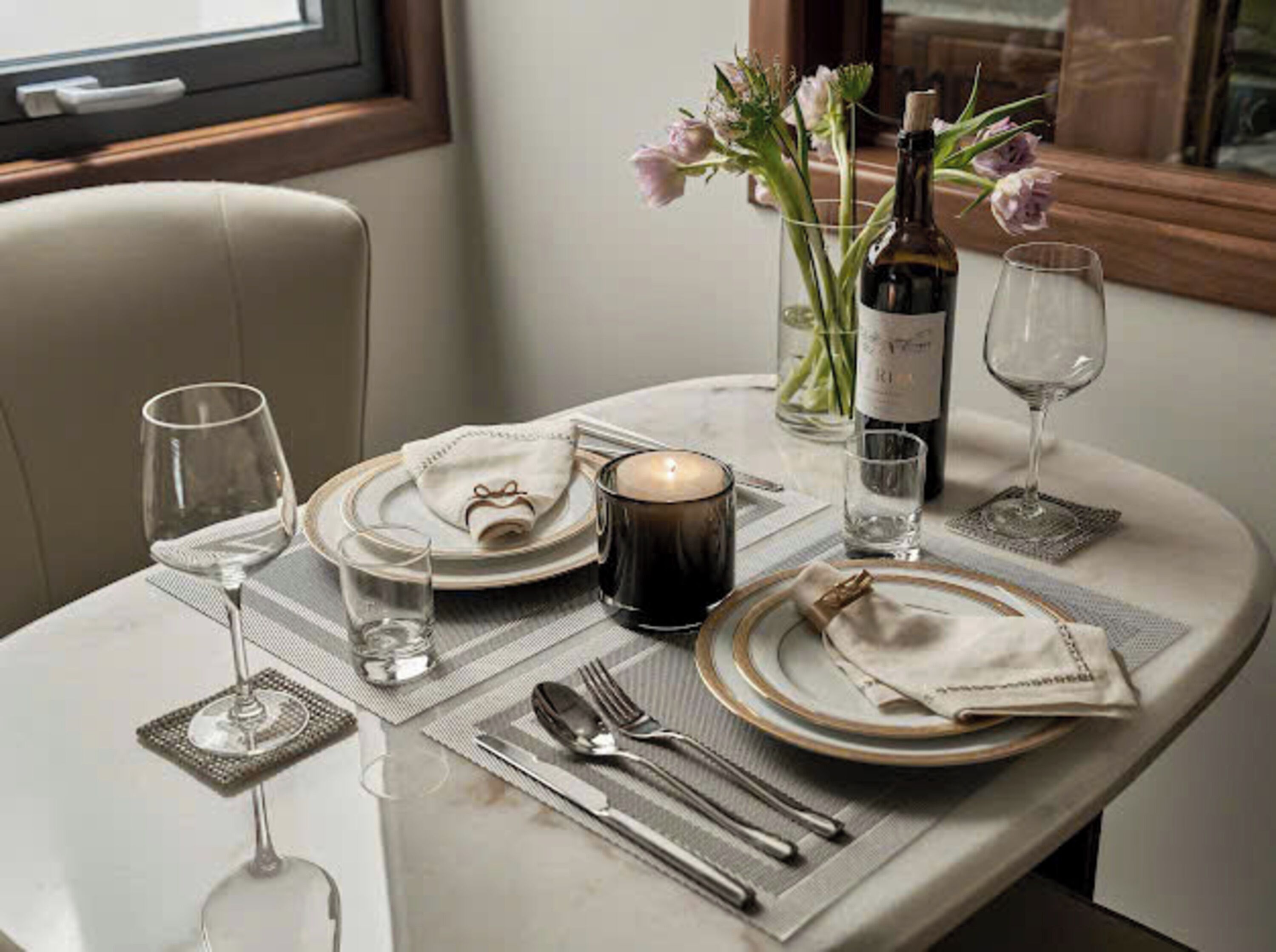 A dining table set with plates, cutlery, glasses, a candle, and a bottle of wine.