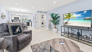 A modern living room with a grey sofa, a coffee table, a TV on a stand, and a kitchen in the background. - Beach, Pool; Las Olas Getaway (Fort Lauderdale)