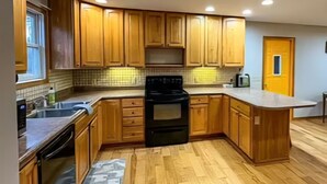 Una cucina con mobili in legno, piano cottura nero e zoccolo in piastrelle.