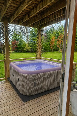 Un bain à remous sur une terrasse en bois, surmontée d’une pergola.