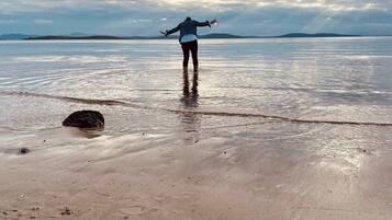 A person standing on a beach with a vast body of water and distant land in the background.