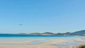 Une plage avec un ciel dégagé, une eau calme et des collines qui se dessinent à l’horizon.