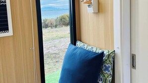 Une pièce avec une fenêtre, un lit recouvert d’une literie à motifs floraux, un tableau accroché au mur et une porte.