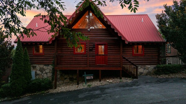 A log cabin with a stone foundation, a red roof, and a porch with a railing. - Sleeps 14 | 3 Kings, Game Room, Hot Tub + 2 Mi to Rocky Top Sports World (Gatlinburg)