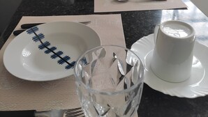 Une table à manger est dressée avec des assiettes, des couverts, un verre et une tasse, et un four à micro-ondes est visible à l’arrière-plan.