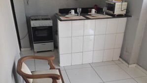 Une cuisine compacte avec des meubles blancs, une cuisinière à gaz et un four à micro-ondes. On y trouve un petit coin repas avec une table ronde et deux chaises en bois.