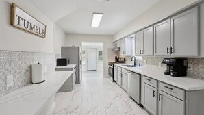 A modern kitchen with white cabinets, a marble floor, and a sign that reads "TUMBLE."
