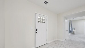 A hallway with a white door, marble flooring, and a white wall.
