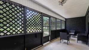 A covered outdoor area with a lattice partition, black chairs, and a concrete floor.