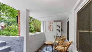A covered outdoor area with a small table and chairs, a blue patterned rug, and a brick wall.