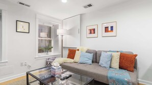 A living room with a grey sofa, a glass coffee table, and a window with a plant.