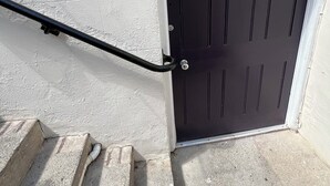 En svart dörr med nummer 7, en skylt som visar vägen till postkontoret och ett svart metallräcke som leder till en trappa av betong.