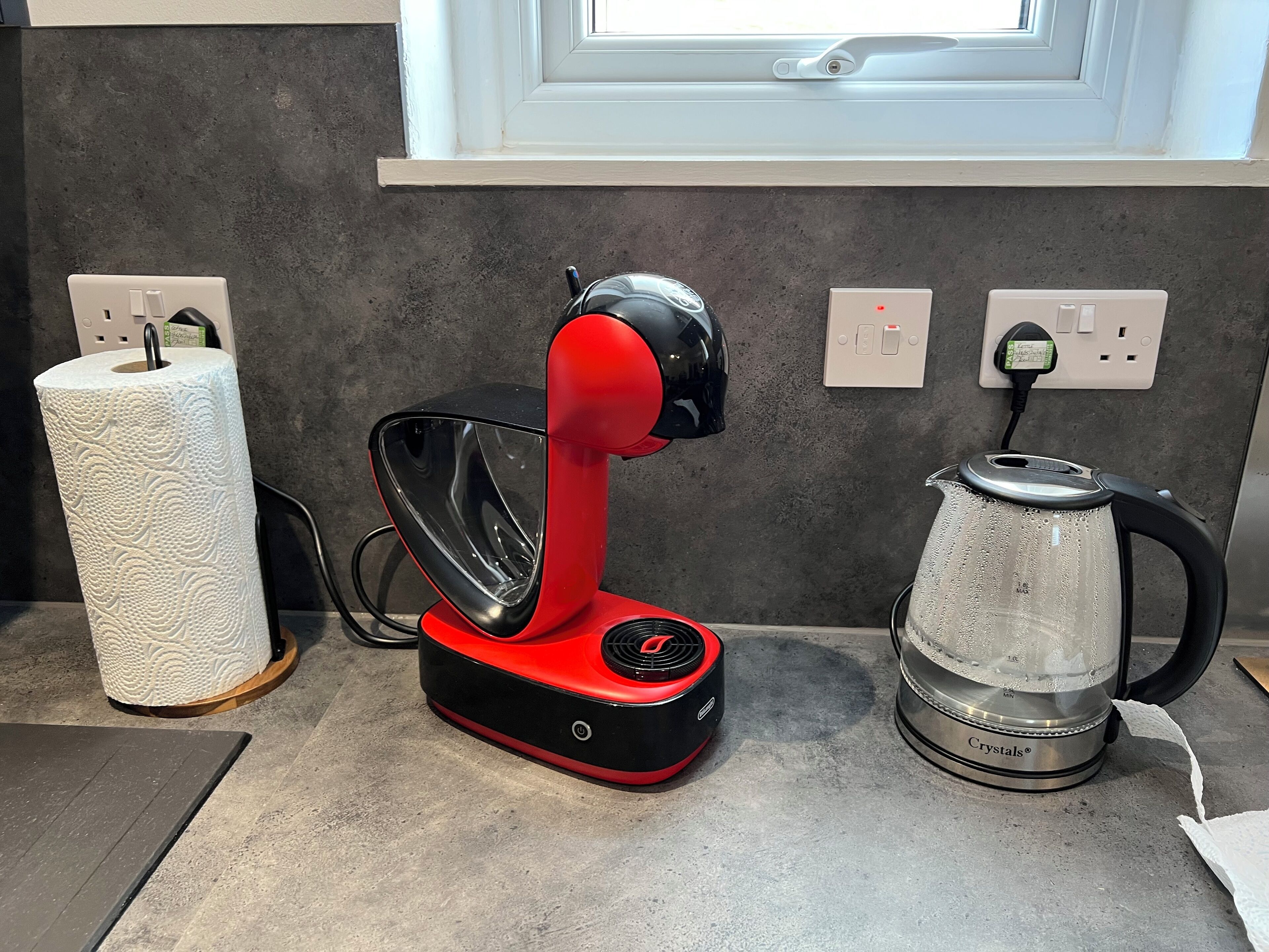 A kitchen with a red electric kettle, a glass water kettle, and a roll of paper towels on the counter.