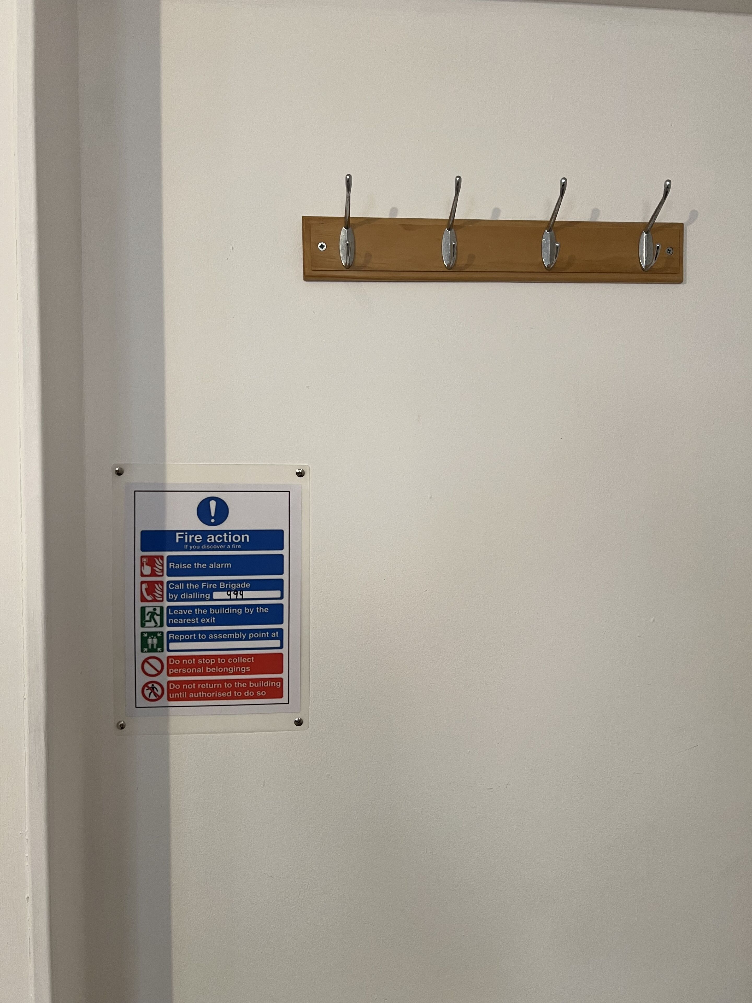 A fire action sign with instructions and a wooden coat rack with hooks.
