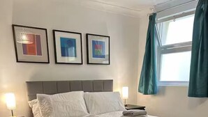 En snyggt bäddad säng med ett gult överkast, två sänglampor och inramade konstverk på väggen.