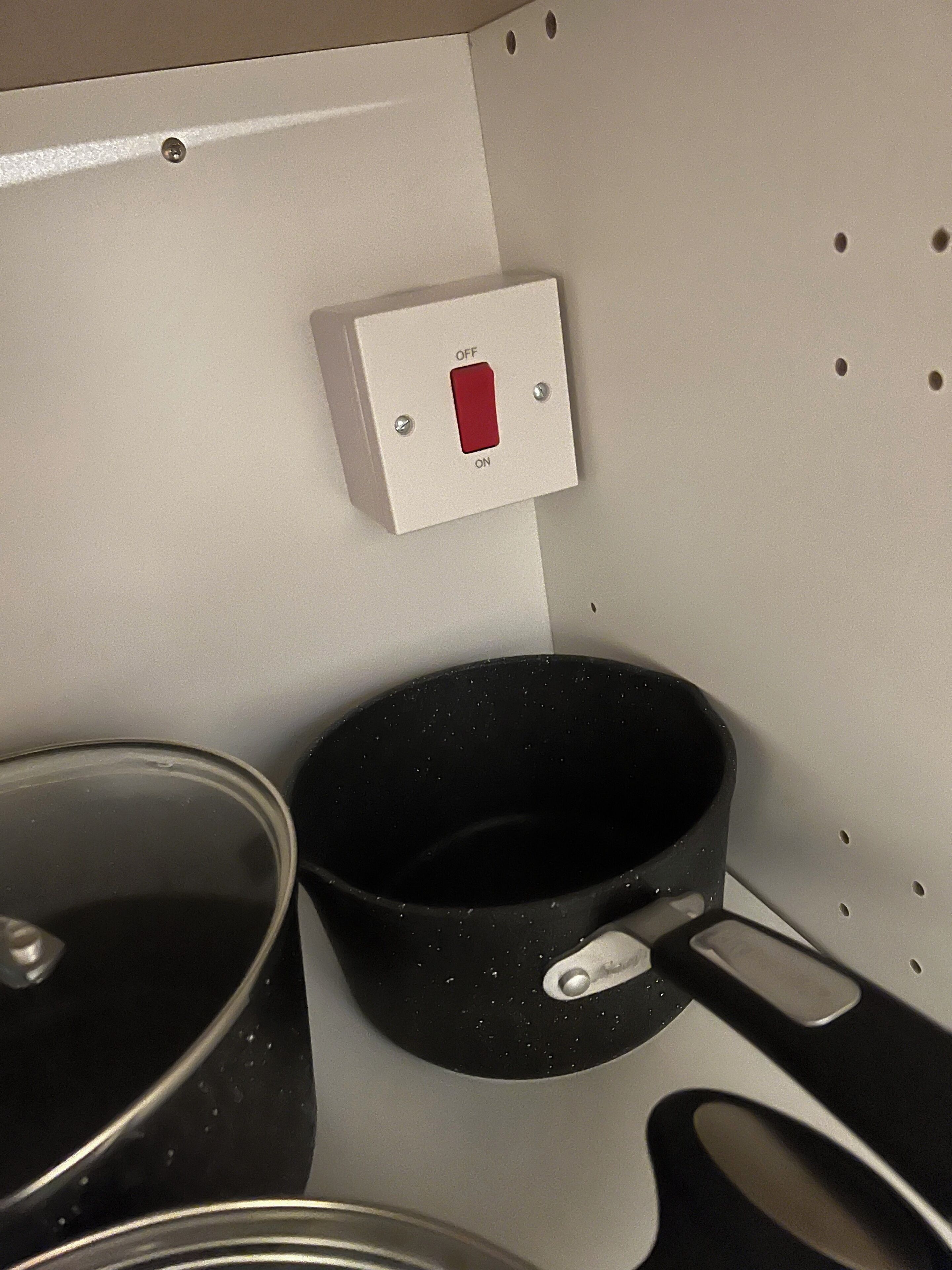 A kitchen area with a white wall, a red power switch, and two black pots.