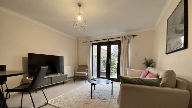 A modern living room with a flat-screen TV, a sofa, a coffee table, and a dining area with chairs. - Comfortable 2 Bedroom House in Bracknell (Bracknell)
