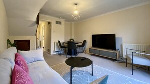 A modern living room with a sofa, a coffee table, a TV, and a dining area with chairs and a table. - Comfortable 2 Bedroom House in Bracknell (Bracknell)