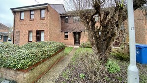 A two-story brick house with a front door, a small garden with a hedge, and a tree in the foreground. - Comfortable 2 Bedroom House in Bracknell (Bracknell)