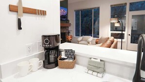 A modern kitchen with a coffee maker, a knife rack, and a cozy seating area with a view of the night sky.