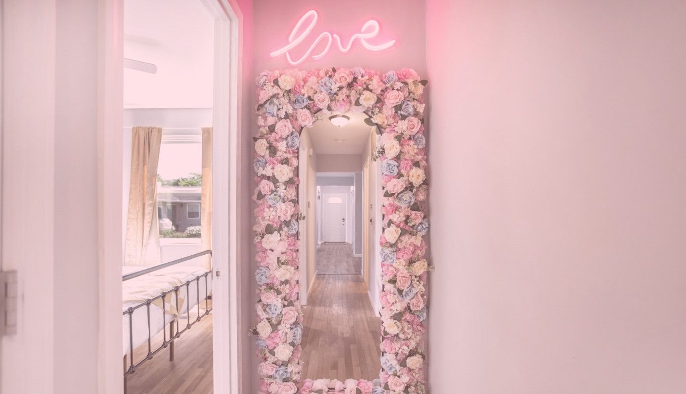 A hallway with a floral mirror and neon 'love' sign.