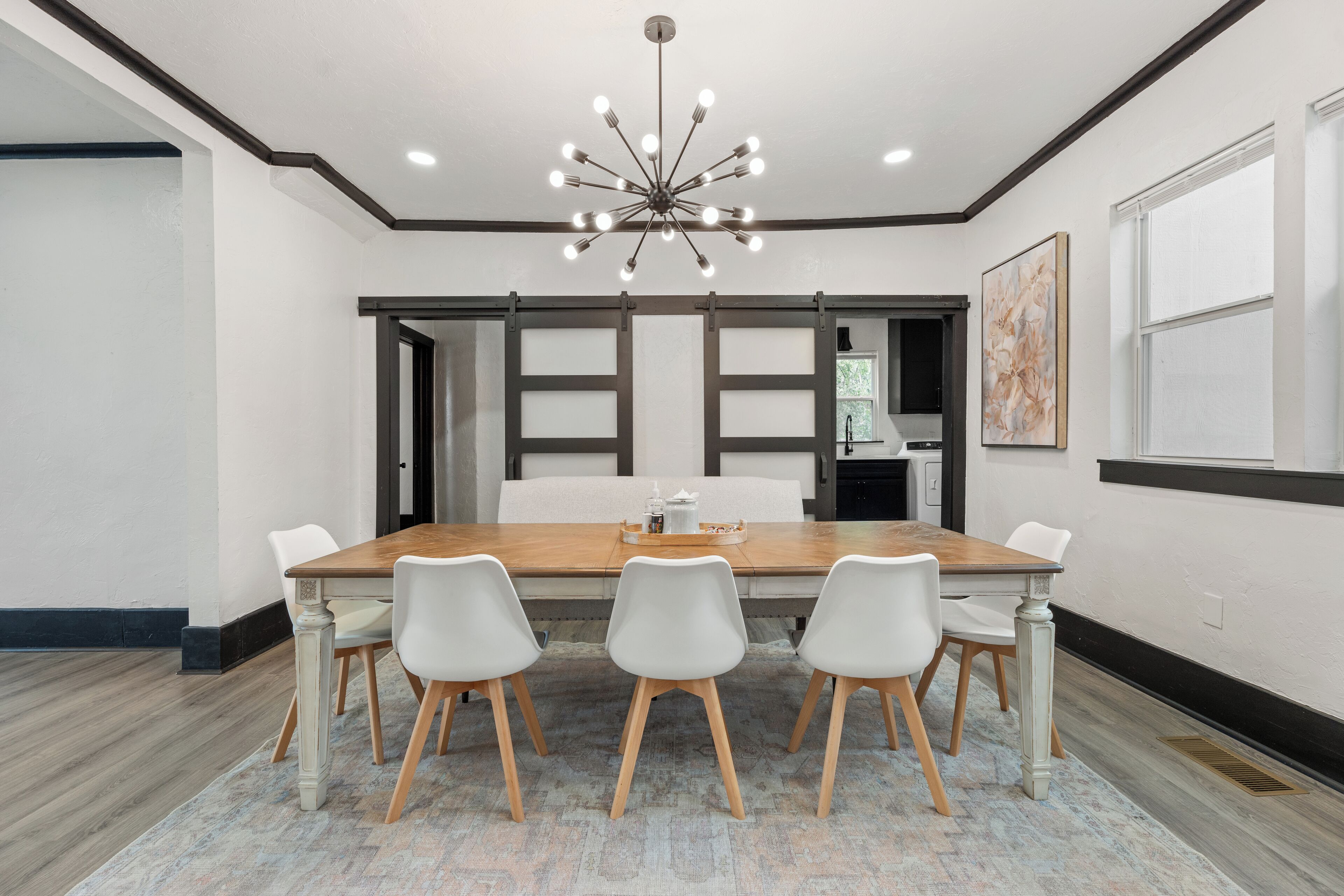 A modern dining room with a wooden table, white chairs, and a chandelier.
