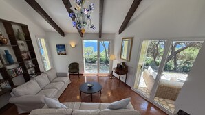 Ein Wohnzimmer mit einer Eckcouch, einem Couchtisch, einer Chandelierleuchtre und Blick durch große Fenster.
