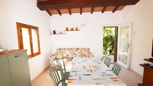 A dining area with a table covered in a tablecloth with fish patterns, a sofa, a cabinet, and a door leading outside.
