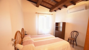 A bedroom with two beds, a wooden wardrobe, a chair, and an air conditioning unit.