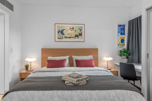 Une chambre d’hôtel avec un lit, deux lampes de chevet, une tête de lit et des œuvres d’art accrochées au mur.