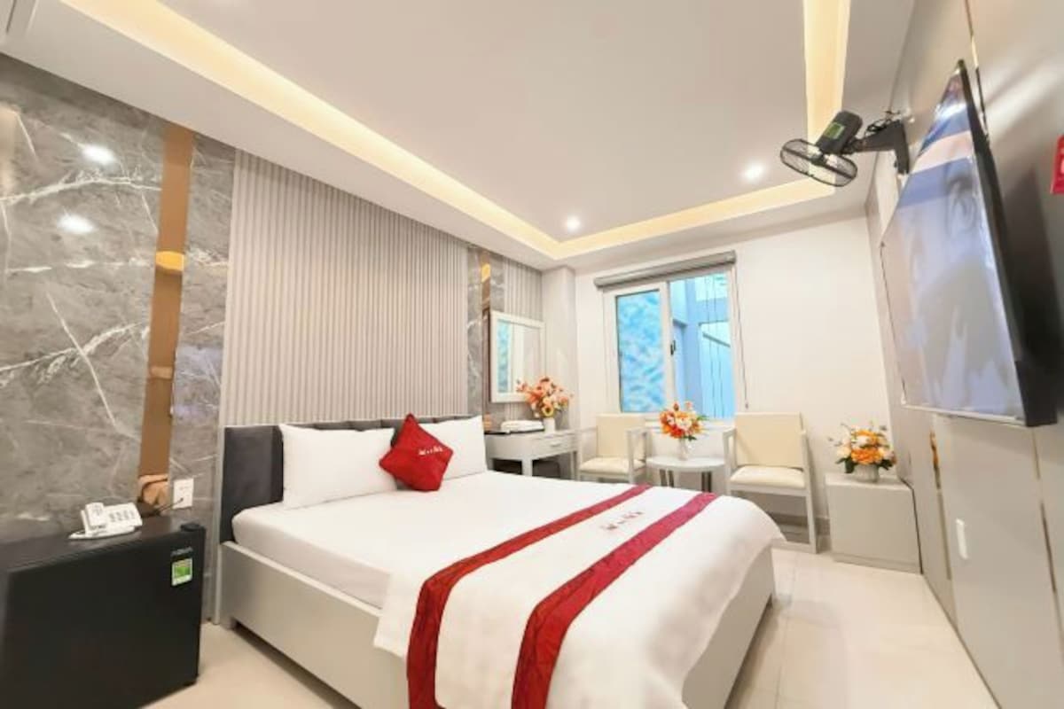 Quarto de hotel moderno com uma cama grande, uma mesa, uma cadeira, uma televisão e uma janela.