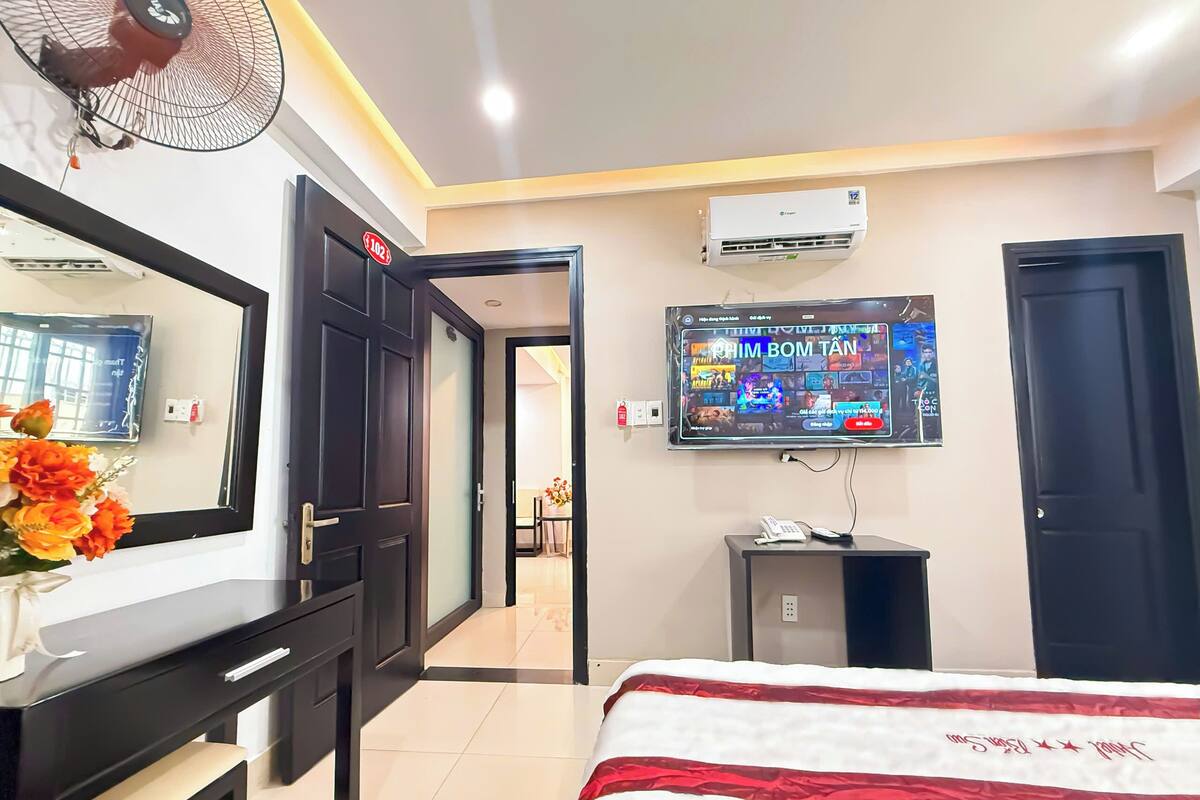 Ein Hotelzimmer mit Bett, Wandfernseher, Schreibtisch mit Spiegel und Ventilator.