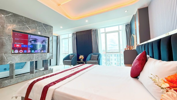 A modern hotel room with a large bed, a flat-screen TV mounted on a marble wall, and a city view through the windows. - Bien Sao Hotel Duong Quang Ham (Ho Chi Minh City)