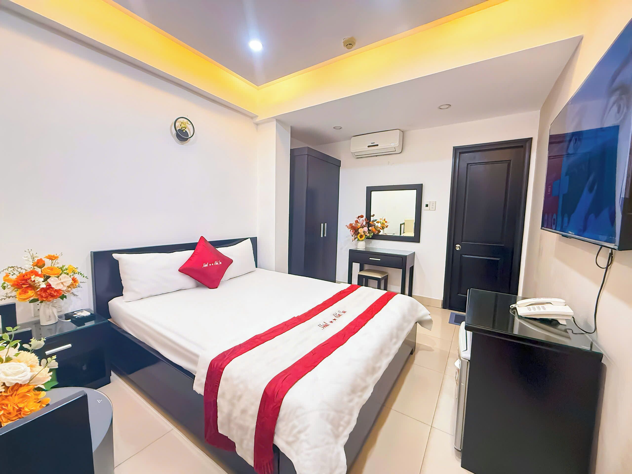 A hotel room with a bed, bedside table, TV, and a desk with a phone.