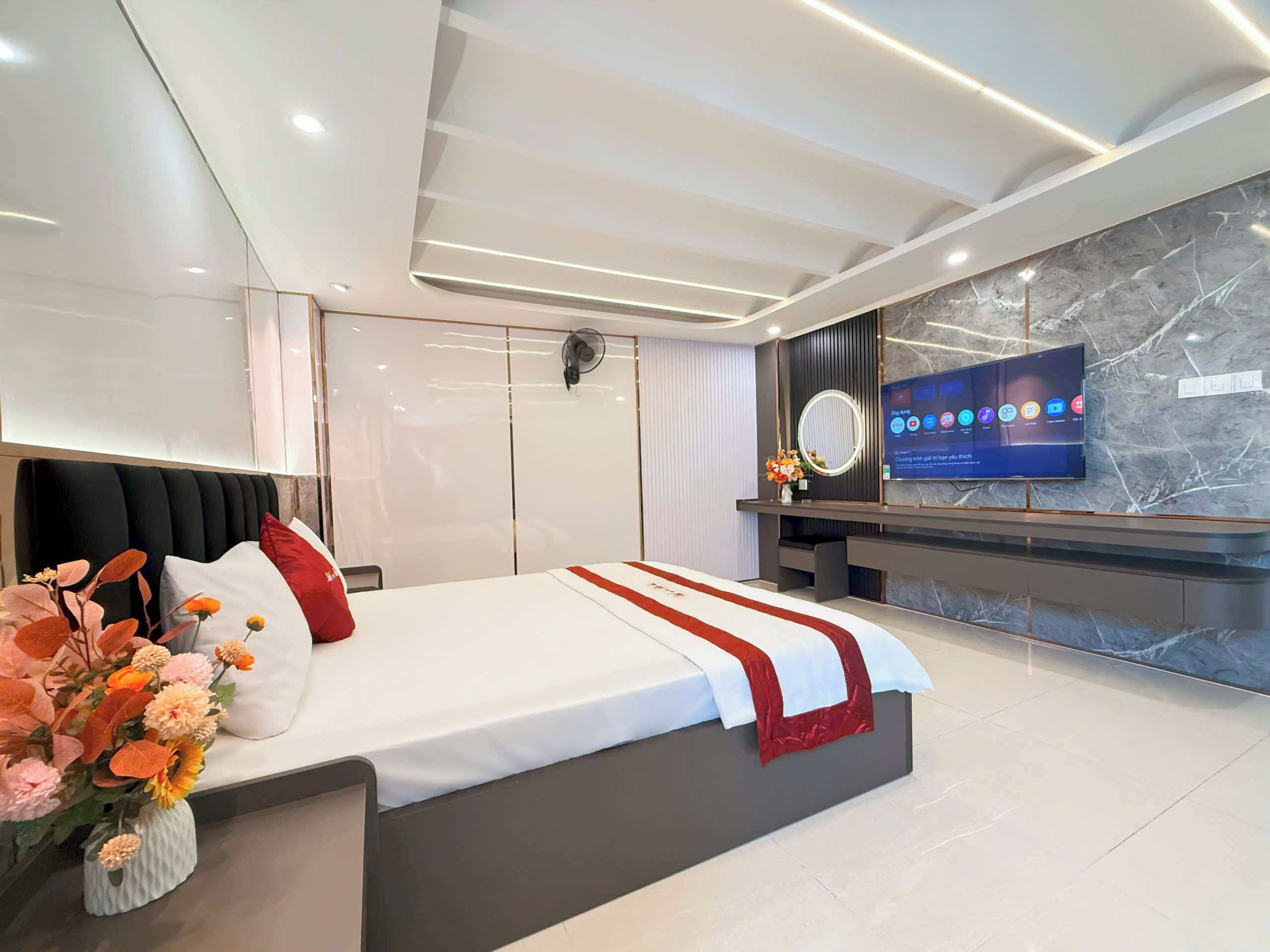 A modern hotel room with a large bed, a TV mounted on the wall, and a marble accent wall.